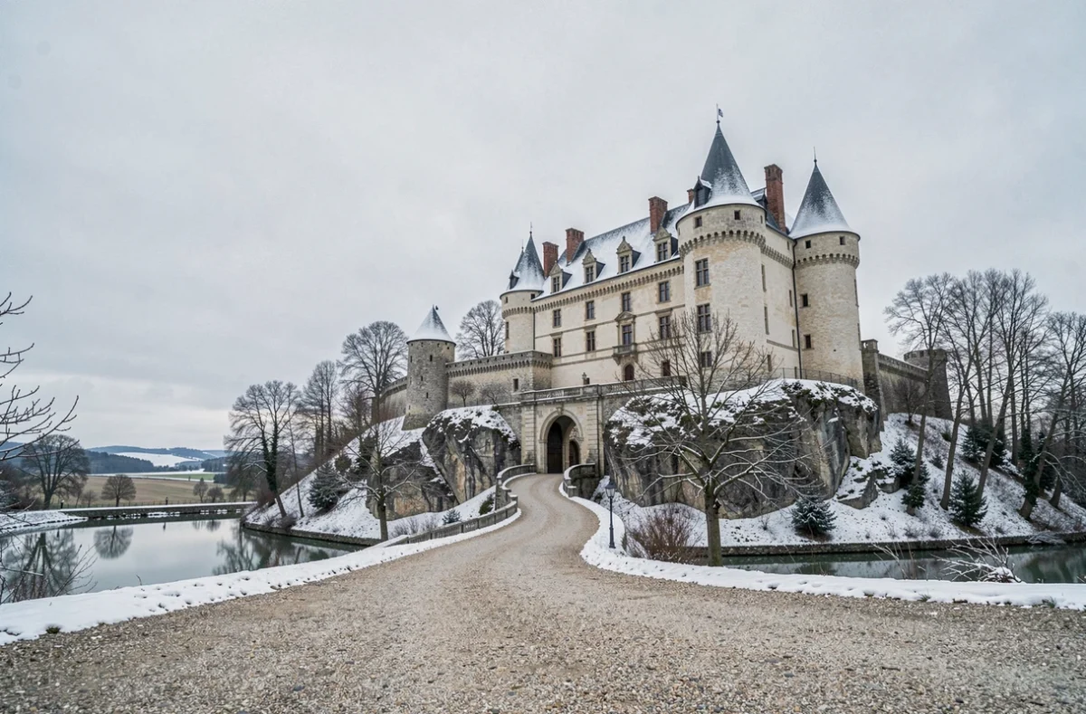 Vue extérieure d'un château fort médiéval français perché sur un rocher sous un ciel hivernal, entouré d'arbres et de neige